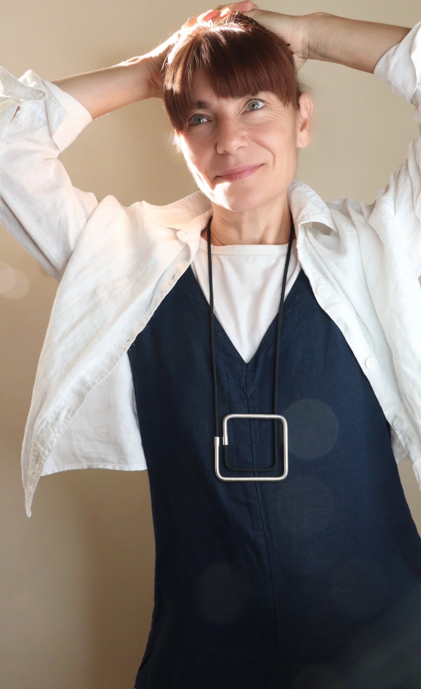 Smiling woman wearing a modern square pendant necklace from FuturisNow's Linea collection with layered white and navy outfits