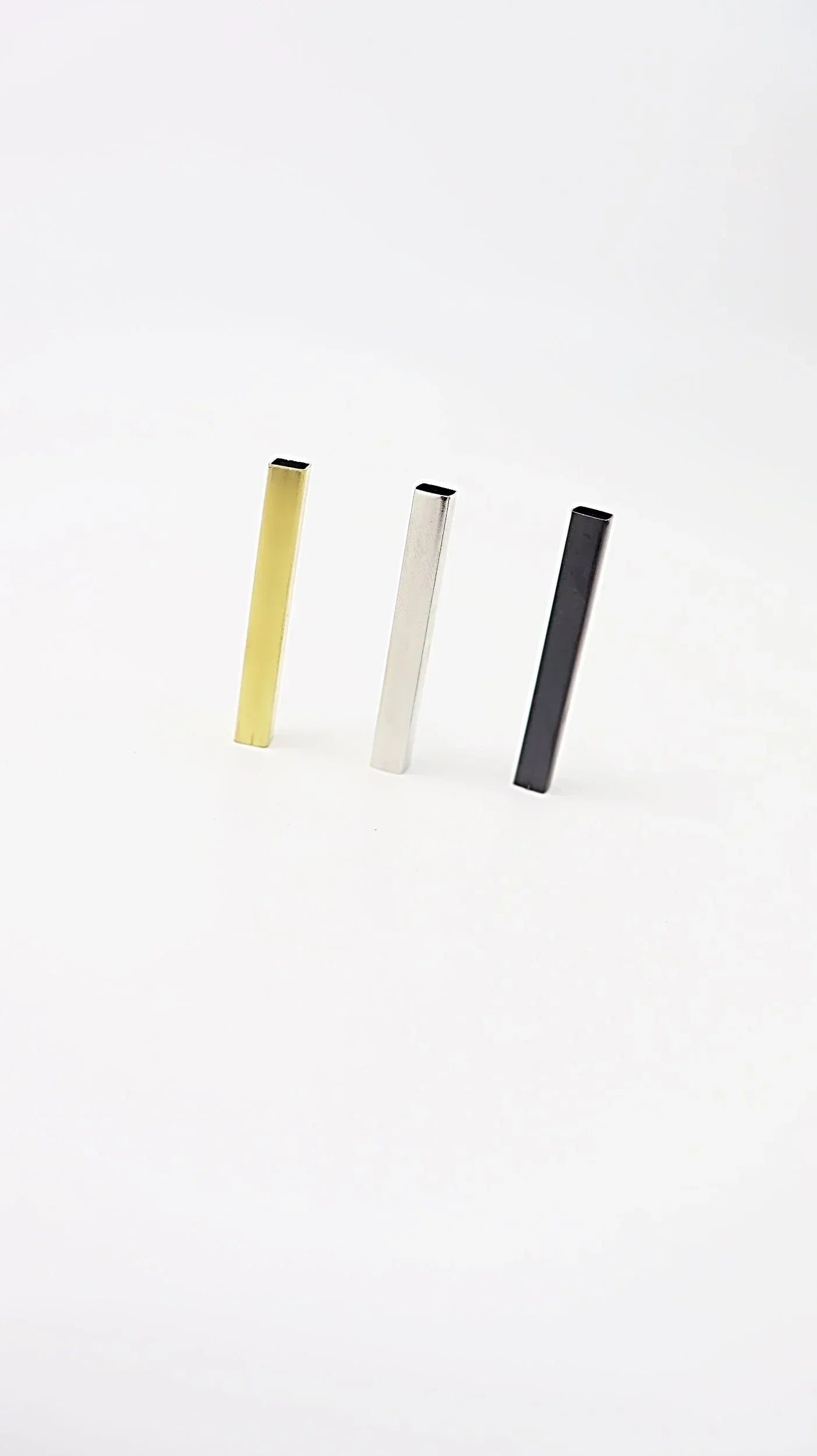 Three vertical tube-shaped jewelry pieces in gold, silver, and black on white background