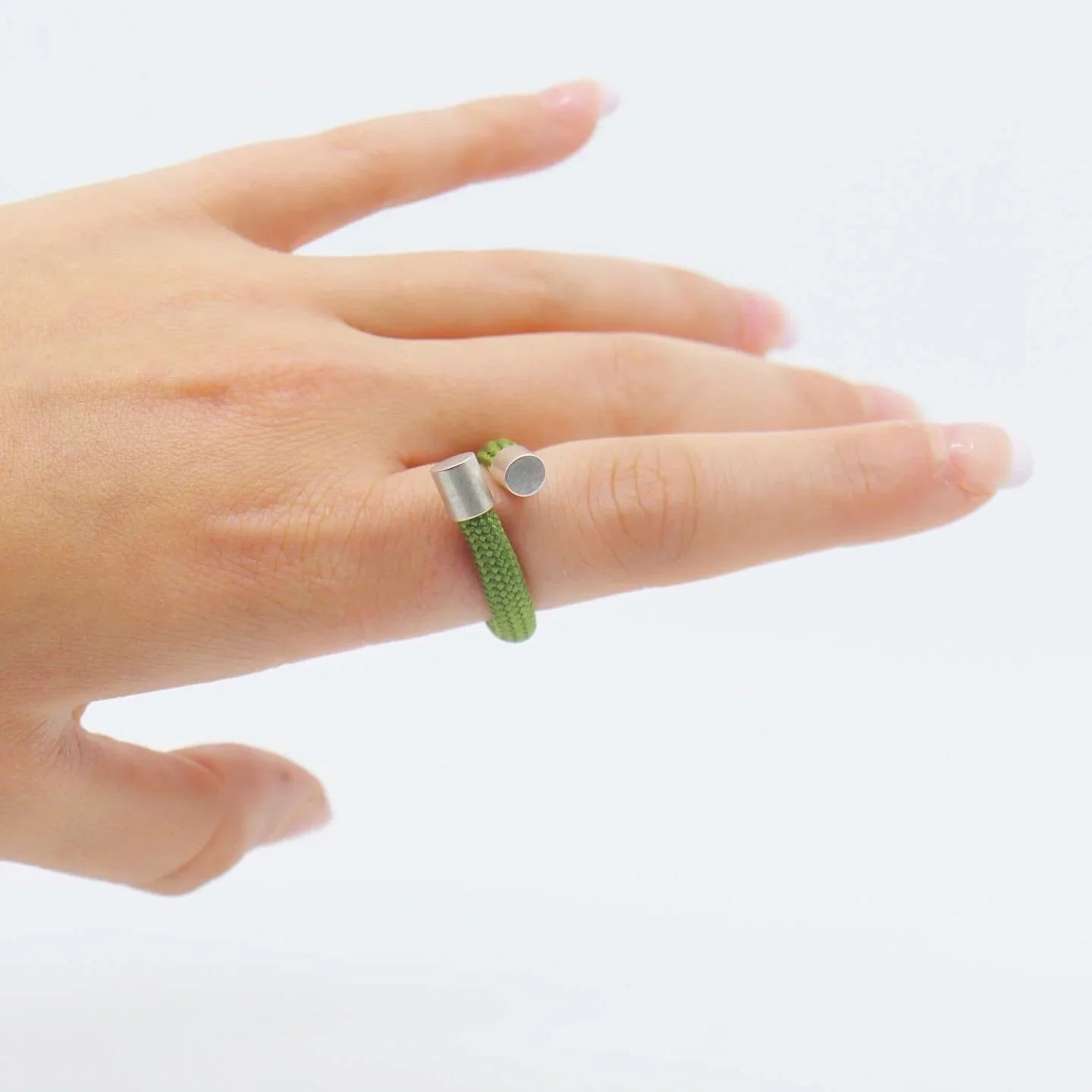 Hand wearing a modern green fabric and silver open-ended ring against a white background