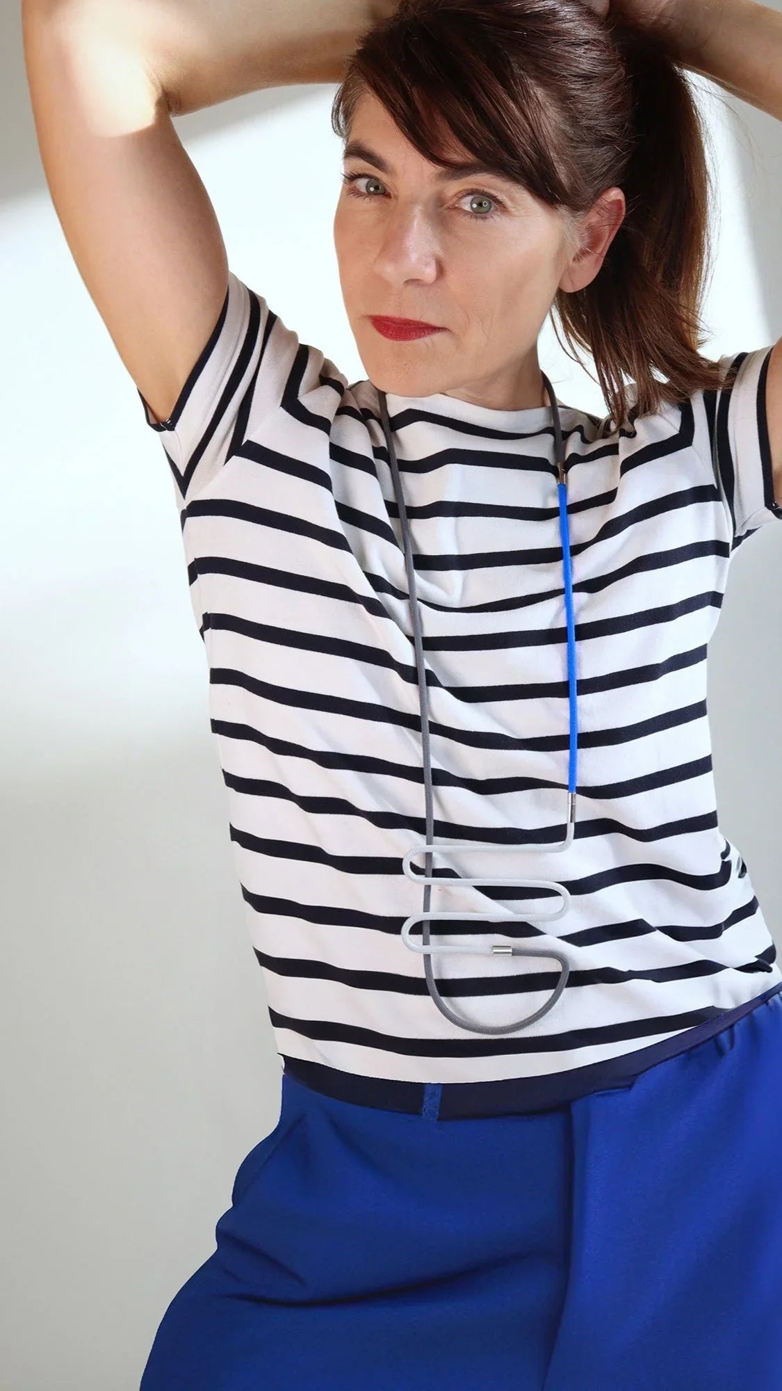 Woman wearing a black and white striped shirt with a blue and gray modern pendant necklace from FuturisNow Linea collection