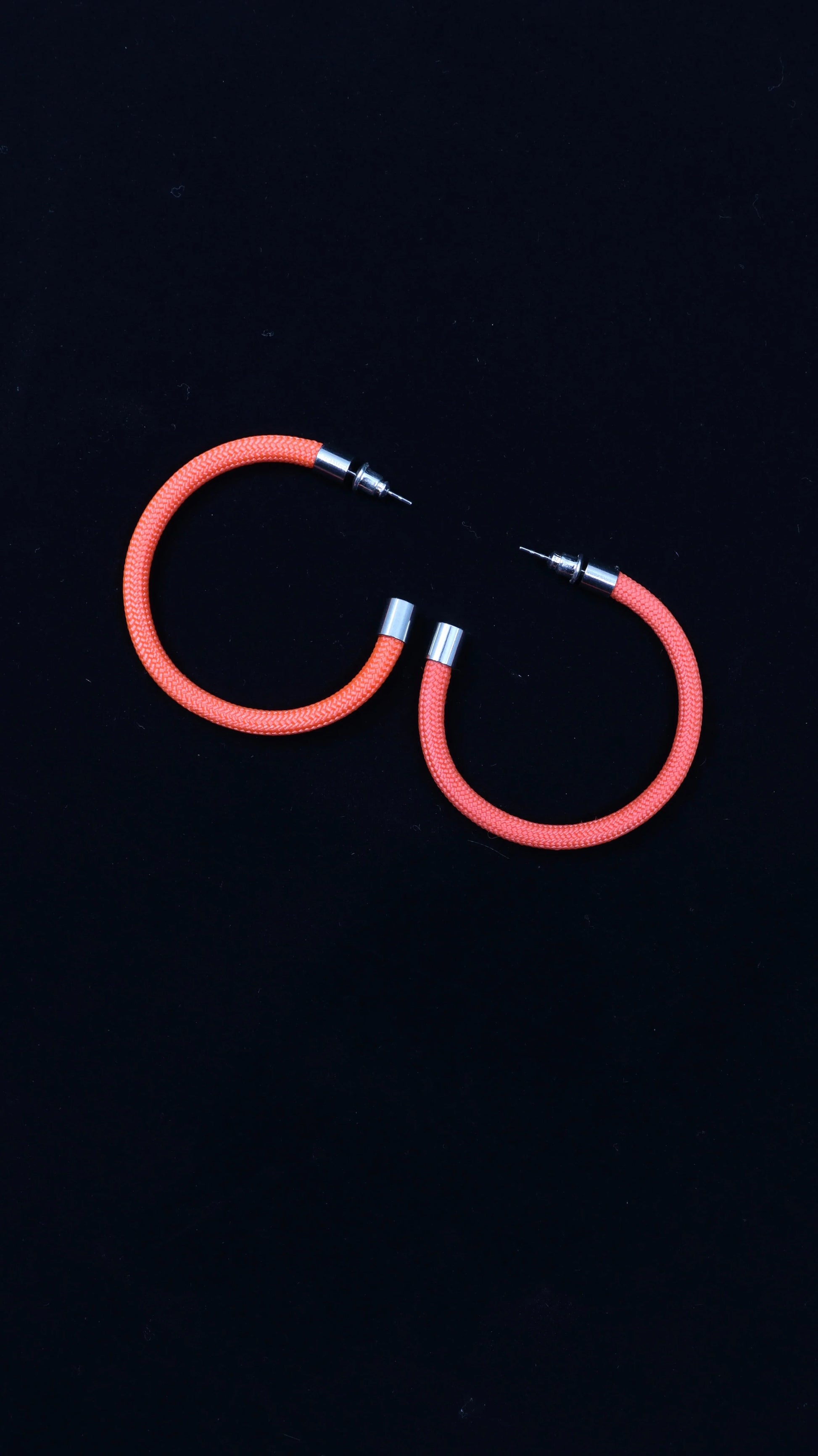 Pair of modern orange hoop earrings with silver metal accents on black background