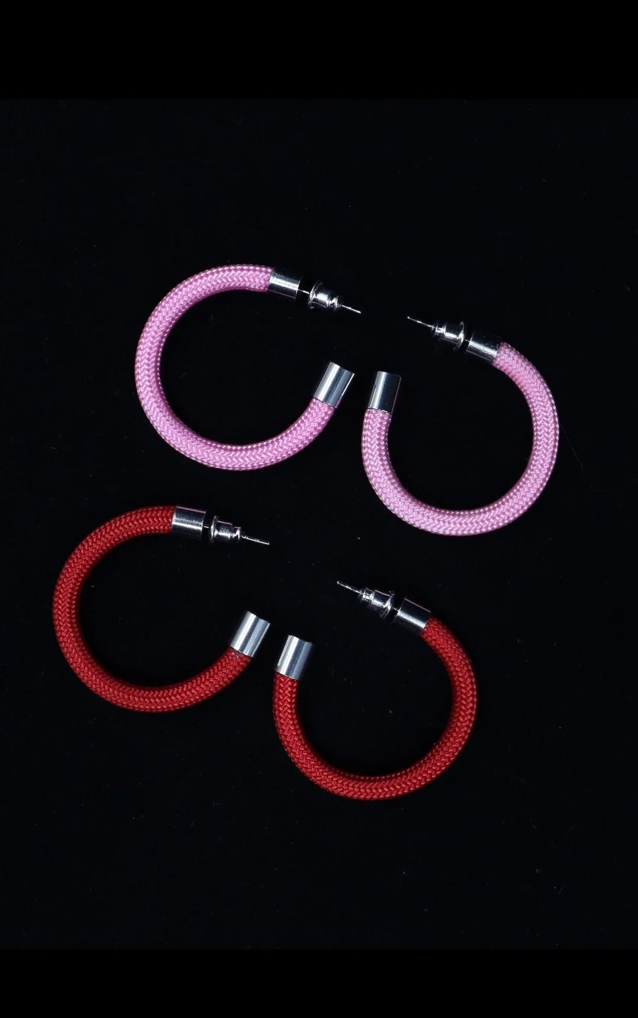 Pair of pink and red hoop earrings with silver metal ends and posts on black background