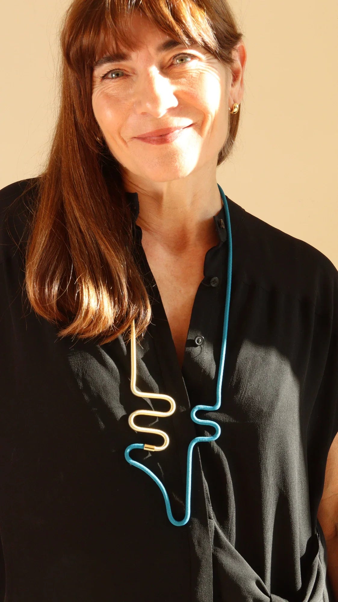 Smiling woman wearing modern, abstract gold and blue Linea collection necklace with black blouse